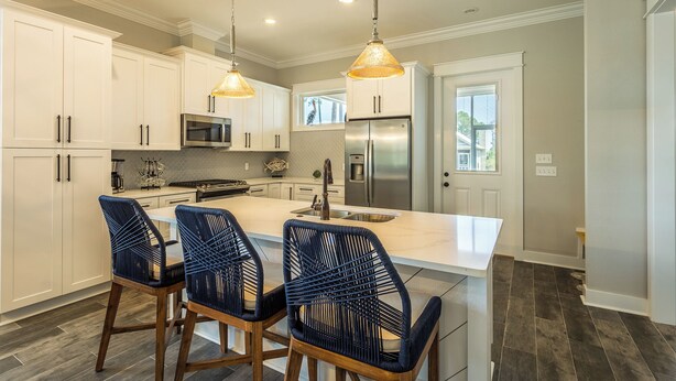 A modern kitchen with white cabinetry, a central island with bar stools, stainless steel appliances, and pendant lighting.