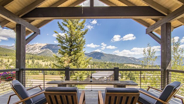 A covered outdoor seating area with a table and chairs, overlooking a mountainous landscape. - Breathtaking Big Sky Luxury Retreat (Big Sky)