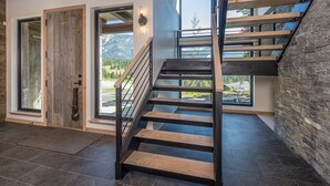 A modern interior with a wooden staircase, large windows, and a stone wall. - Breathtaking Big Sky Luxury Retreat (Big Sky)
