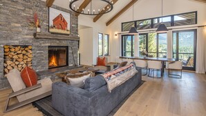 A spacious living room with a stone fireplace, a large gray sectional sofa, and a dining area with a long table. - Breathtaking Big Sky Luxury Retreat (Big Sky)