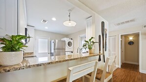 Une cuisine moderne dotée de plans de travail en granit, de meubles blancs et d’un lave-linge encastré.