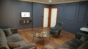 Una sala de estar moderna con paredes oscuras, suelo de madera y muebles grises.