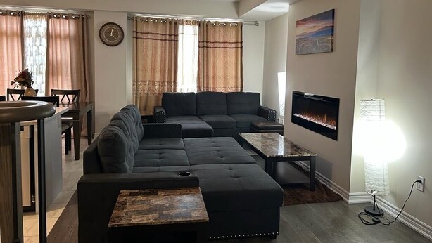 Ein Wohnzimmer mit einer Eckcouch, einem Flachbildfernseher, einem Kamin und einem Essbereich mit Tisch und Stühlen.