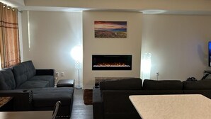 Ein modernes Wohnzimmer mit Kamin, einer großen Couch, einem Esstisch und einem Bild an der Wand.