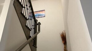 Eine Treppe mit dunkler Holzhandläufe und schwarzen Spindeln, die zu einer Empore führt, auf der ein gerahmtes Bild eines Sonnenuntergangs über dem Meer zu sehen ist.