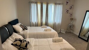 Ein Hotelzimmer mit zwei Betten, beiger Bettwäsche, einem schwarzen Kopfteil und einem großen Spiegel.