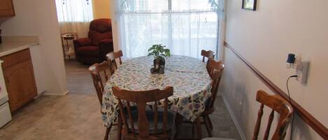 Un comedor con una mesa redonda cubierta con un mantel floral, rodeado de sillas de madera con asientos acolchados.