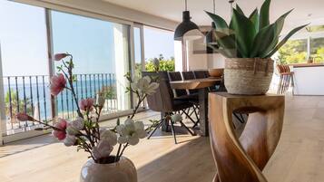 Een moderne eetruimte met uitzicht op zee, een houten eettafel, stoelen en een potplant.