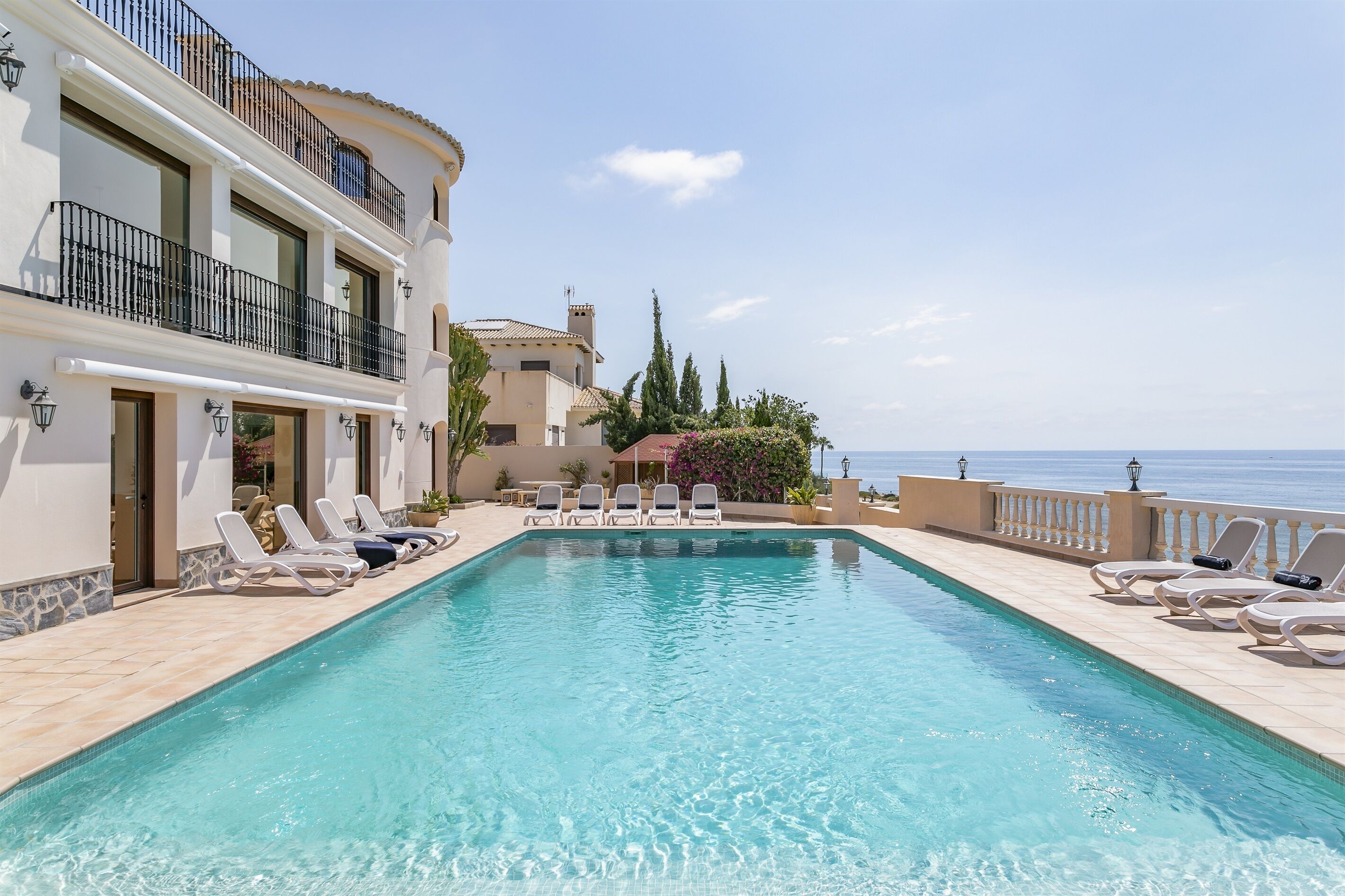 Zona junto a la piscina con sillones de descanso y vista al mar.