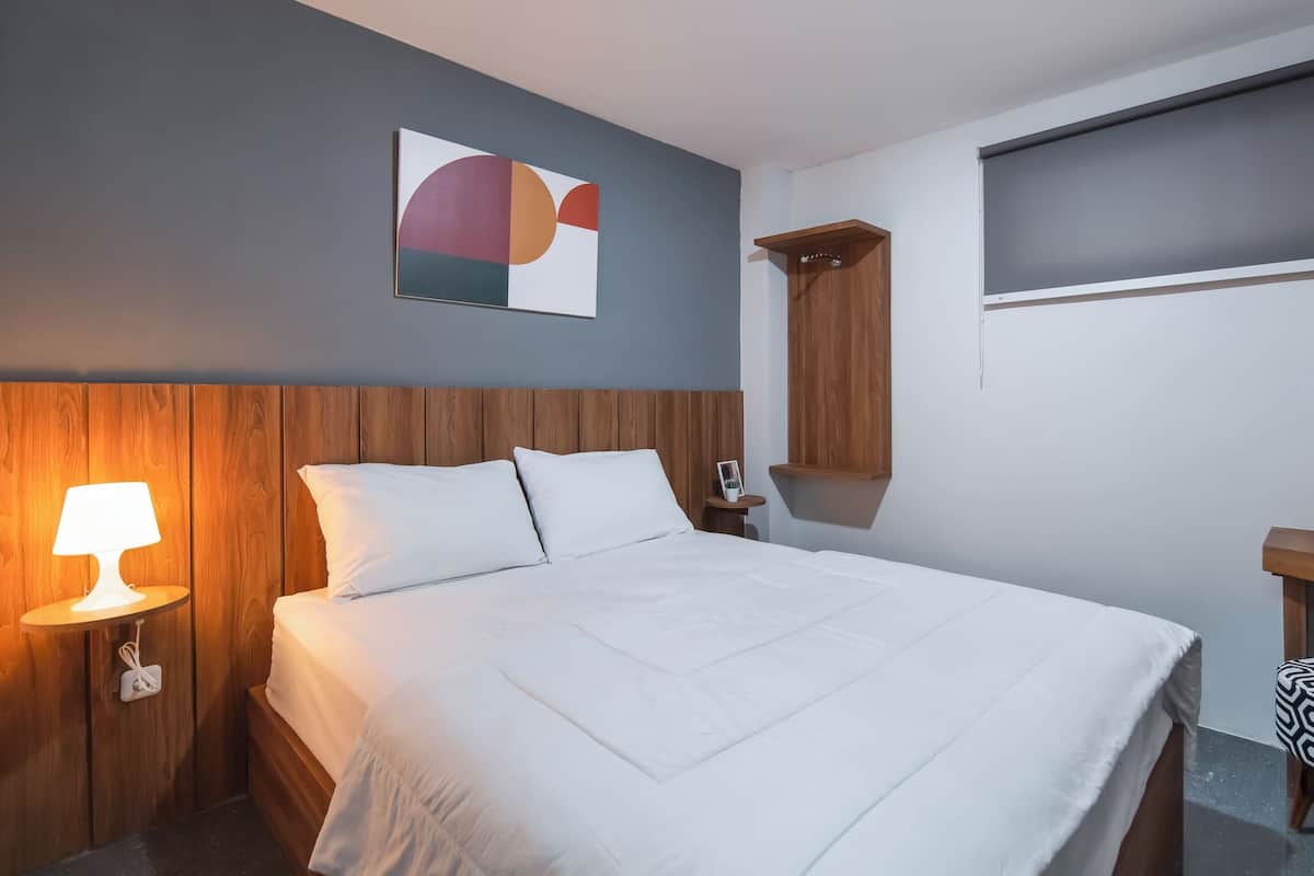 Un lit bien fait, avec une literie blanche, une tête de lit en bois, une lampe de chevet et une étagère fixée au mur.