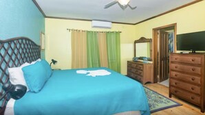 Een slaapkamer met een bed, dressoir, spiegel en plafondventilator.