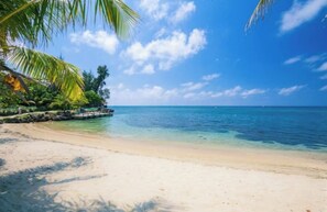A beach with clear turquoise water, white sand, and palm trees. - BEST LOCATION next to West Bay Beach / Beachfront Condo steps away from West Bay (Roatan)