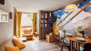 En hyggelig stue med en sofa, et spisebord dækket til to personer, og en trappe til et loftplan.