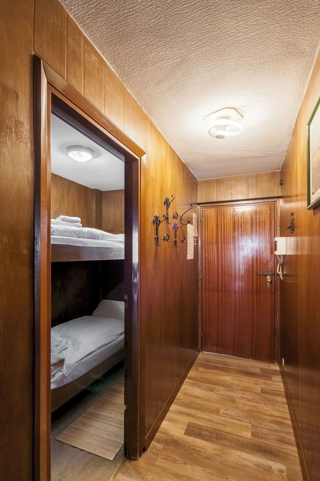 Una habitación de madera con literas, una puerta de madera y una lámpara en el techo.