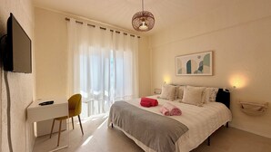Un dormitorio con cama, mesitas de noche, un escritorio, una silla, televisor y ventana con cortinas.
