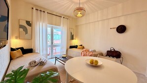 Una habitación de hotel moderna con una cama, una mesa redonda de comedor, una mesita con una computadora portátil, una maleta y una planta.