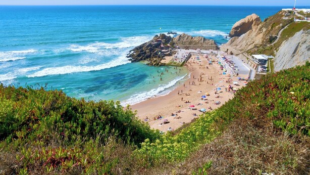 Una playa costera con acantilados rocosos, una playa de arena y un muelle que se adentra en el mar.