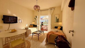 Un espacio habitable compacto con una mesa de comedor, un sofá, un televisor montado en la pared y vistas al exterior a través de una ventana.