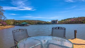 Vista para o lago com mesa e cadeiras de vidro, um cais e um edifício do outro lado da água.