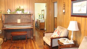 A room with a wooden floor, a piano, a chair with a cushion, a lamp, and a framed picture on the wall. - Relaxing, quiet country setting. Close to many Mountain activities! (Sugar Grove)