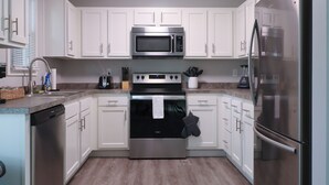 Una cocina moderna con armarios blancos, electrodomésticos de acero inoxidable y piso de madera.