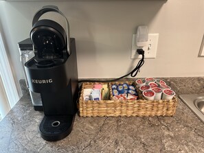 Una cafetera Keurig sobre una encimera de cocina, junto a un cesto de cápsulas de café y otra máquina de café.