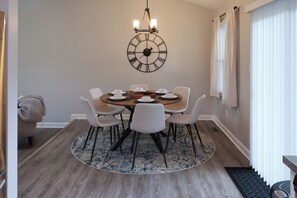 A dining area with a round table, white chairs, a wall clock, and a chandelier.
