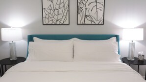 Una cama con ropa blanca, dos mesitas de noche con lámparas y dos obras de arte colgadas en la pared.