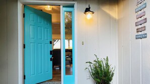 A turquoise door opening to a room with a welcome mat, a potted plant, and motivational signs on the wall.