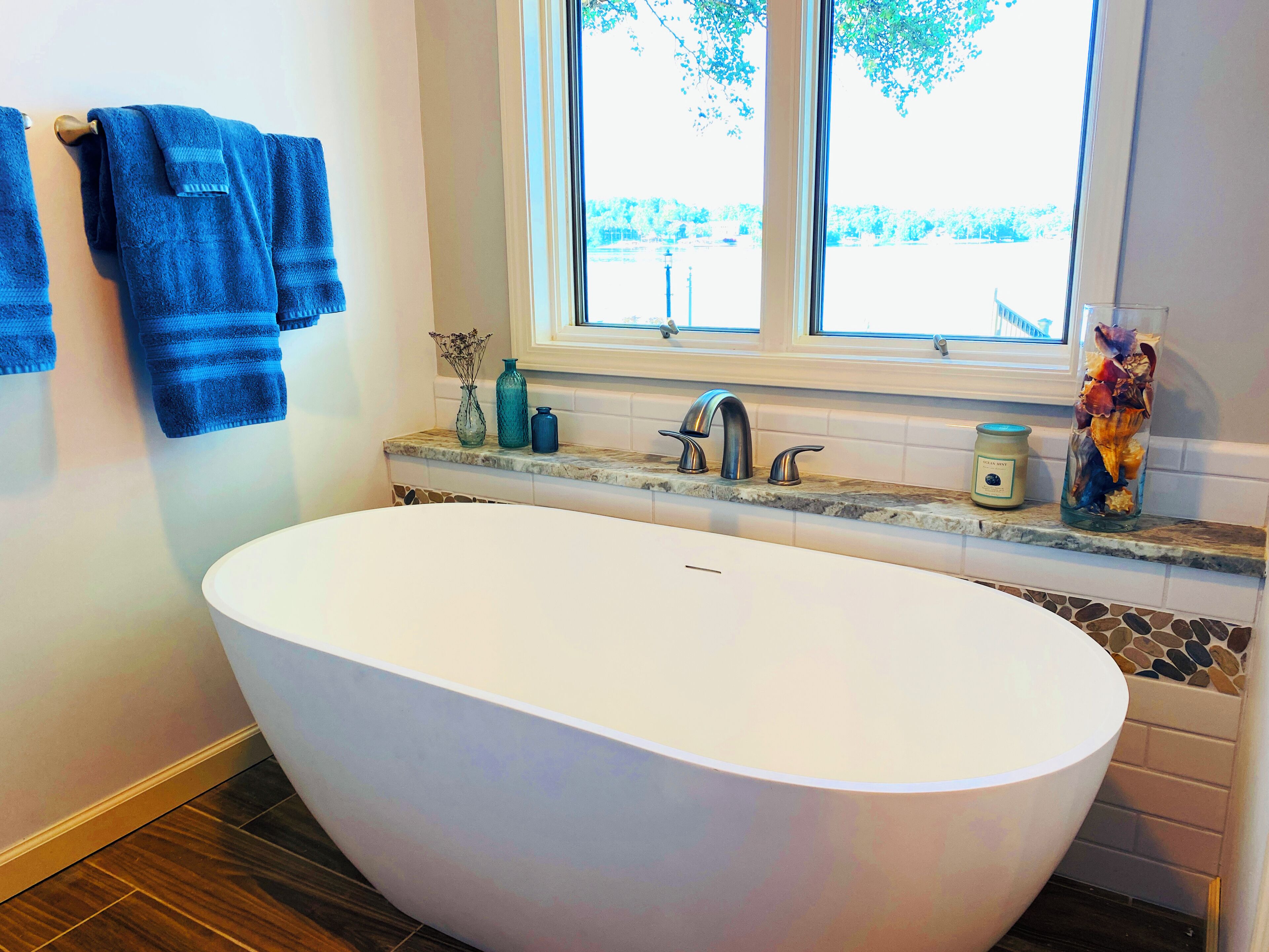 A modern bathroom with a freestanding bathtub, a window with a view, and a countertop with a vase and candle.