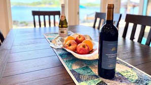 A table with a bottle of Montepulciano d'Aprii wine, a plate of fruit, and a placemat with a coastal view.