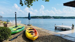 A lakeside dock with kayaks, a lounge chair, and a potted plant.