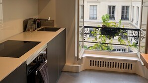 A modern kitchen with a large window, a built-in oven, and a view of a balcony with greenery. - Très bel Appartement Familial Parisien aux Pieds des Invalides (Paris)