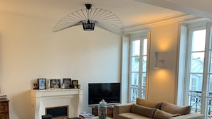 A modern living room with a large sectional sofa, a flat-screen TV, a fireplace, and large windows. - Très bel Appartement Familial Parisien aux Pieds des Invalides (Paris)