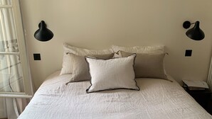 A neatly made bed with white bedding and two pillows, flanked by two black wall sconces. - Très bel Appartement Familial Parisien aux Pieds des Invalides (Paris)