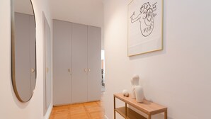 A hallway with a wooden floor, a white wardrobe, a round mirror, and a framed artwork on the wall.