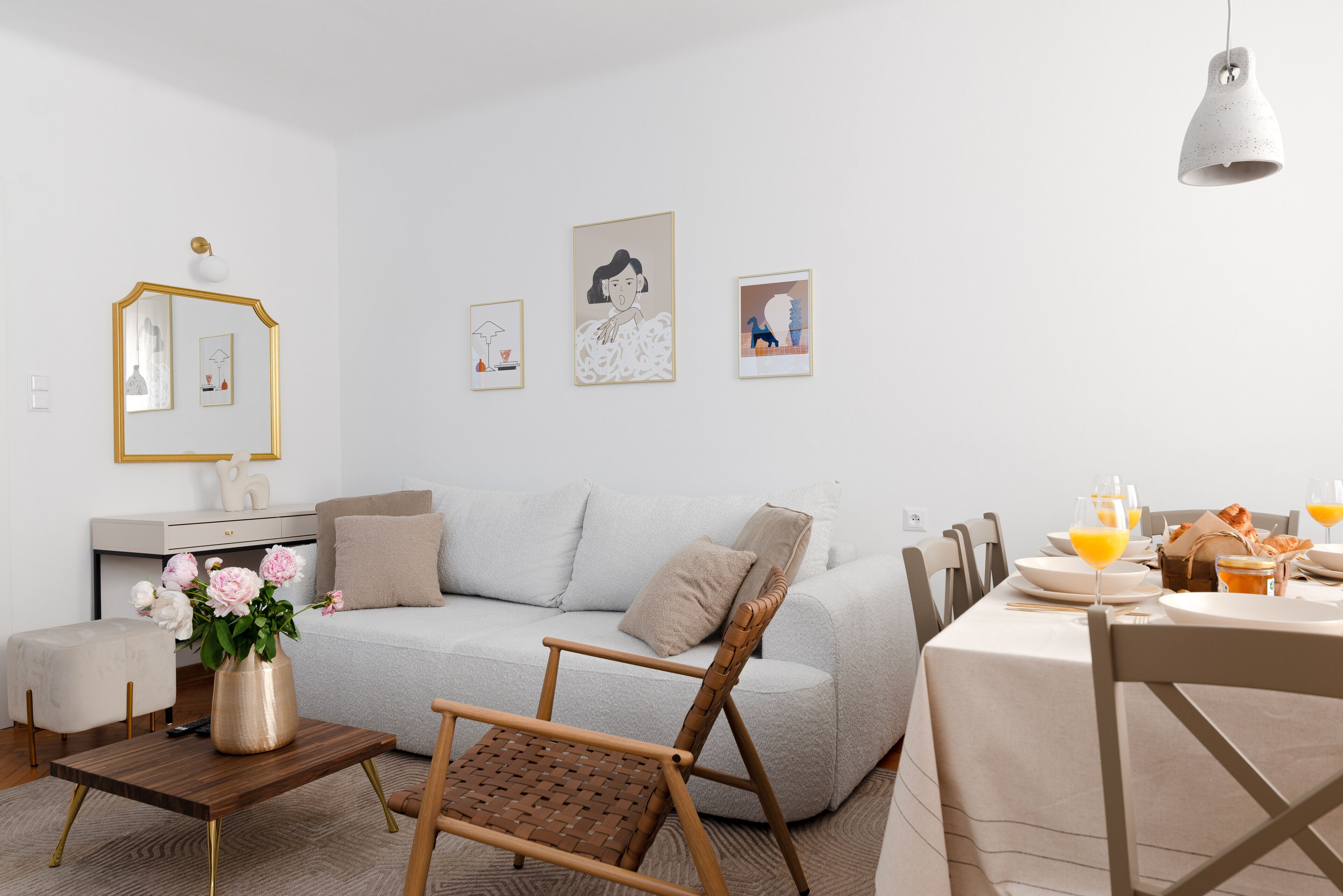 A modern living room with a sofa, a coffee table, a chair, and a dining table set for breakfast. There are framed artworks on the wall.