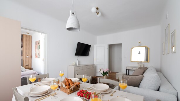 A modern dining area with a white table set for breakfast, including plates, glasses, and a basket of bread.