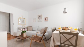A modern living room with a sofa, a dining table set for breakfast, and a coffee table with flowers.