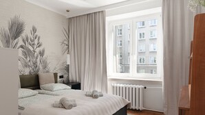 A bedroom with a large bed, a radiator, a window with curtains, and a wall with a plant mural.
