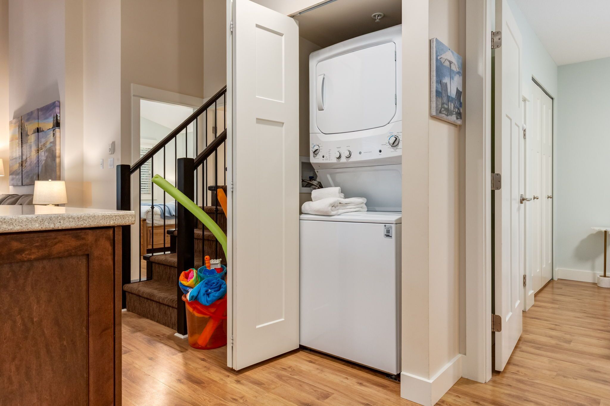 A laundry room with a washer and dryer, a staircase, and a colorful toy bin.