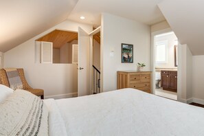 Une chambre à coucher avec un grand lit, une chaise en bois, une commode et un tableau accroché au mur.