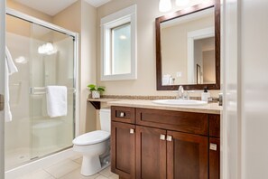 Une salle de bain moderne avec une douche à l’italienne en verre, des toilettes blanches, un meuble-lavabo en bois et un grand miroir.
