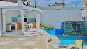 A modern outdoor kitchen area with a dining set, a pool, and a sun lounger. - Villa Mar Azul (Manta)