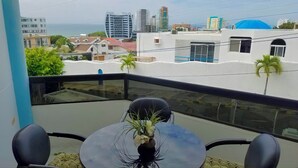 A balcony with a table and chairs, overlooking a cityscape with buildings and palm trees. - Villa Mar Azul (Manta)