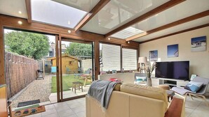 A spacious living room with a large sliding glass door leading to a backyard, a comfortable sofa, a flat-screen TV, and a dining area.
