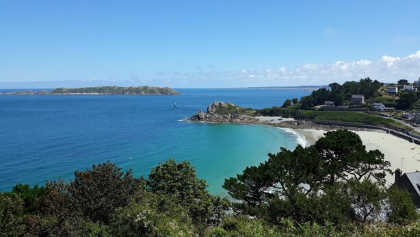 A coastal view with a beach, rocky outcrops, and a lighthouse.