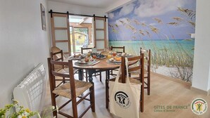 A dining area with a table set for breakfast, chairs, a radiator, and a beach mural on the wall.