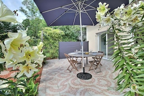 A patio with a round table and chairs, surrounded by a tiled floor and a large umbrella.