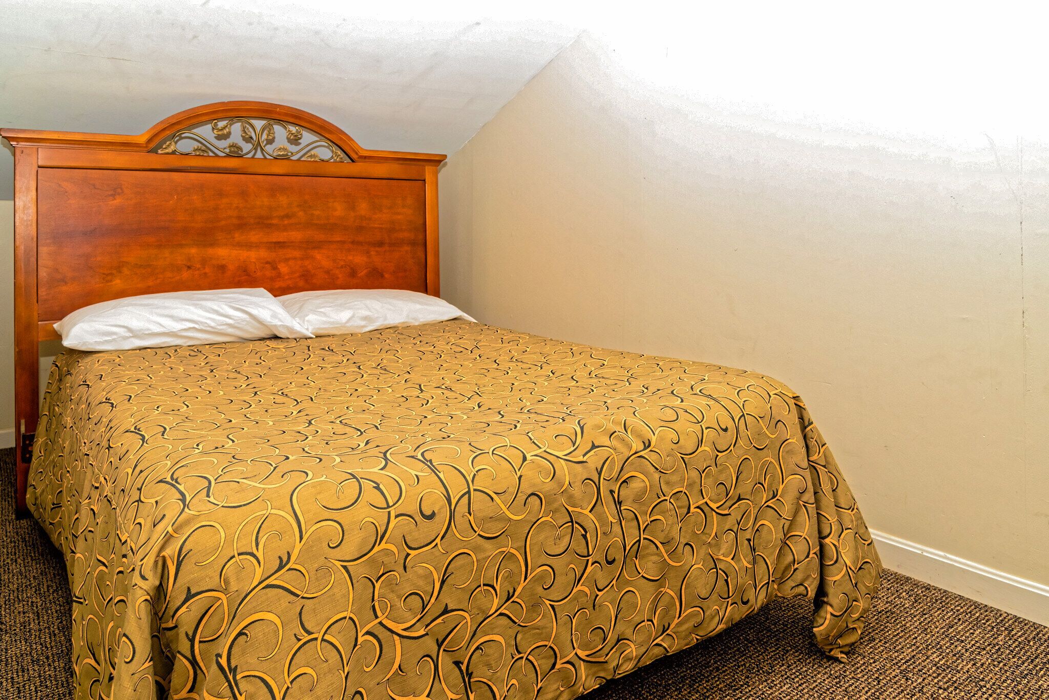 A neatly made bed with a patterned bedspread, a wooden headboard, and a plain wall.